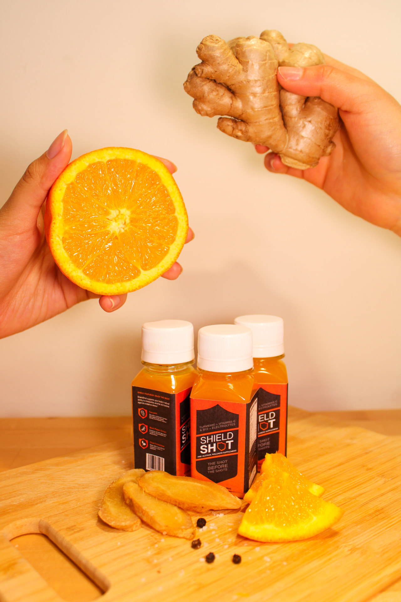 Hands holding orange and ginger above ShieldShot bottles
