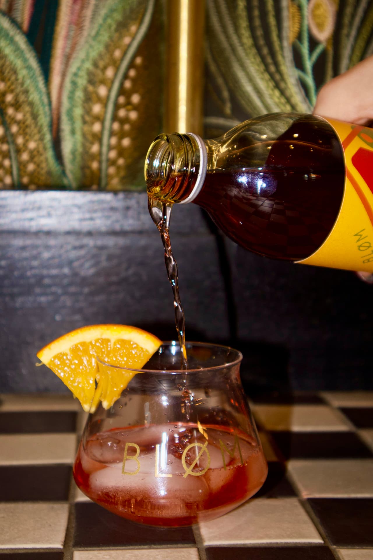 Pouring Bløm Aperitivo into a branded glass